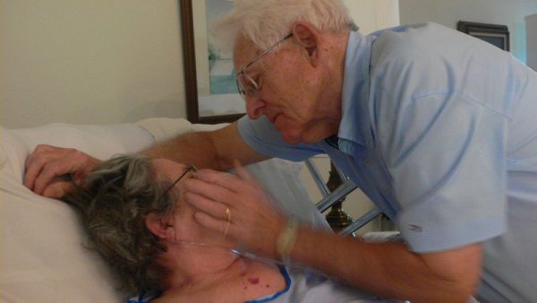Photo of a man touching his wife's face while she lays in a hospital bed.