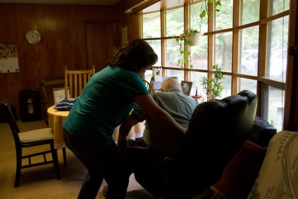 A woman helps an elderly man get up from his chair