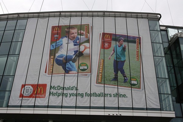 A banner with a McDonald's advertisement on the side of Wembley Stadium. The advertisement features a child kicking a soccer ball and a woman coaching on a grass field.